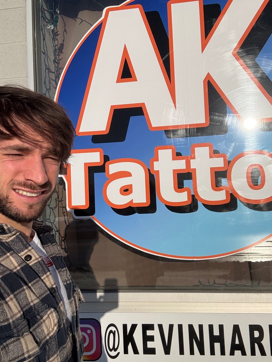 Cade Bennett in front of AK Tattoo sign Anchorage Alaska — tattoo artist 907