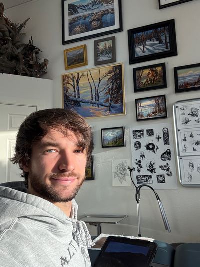 Cade Bennett tattoo artist at AK Tattoo Anchorage Alaska — station with Alaska paintings