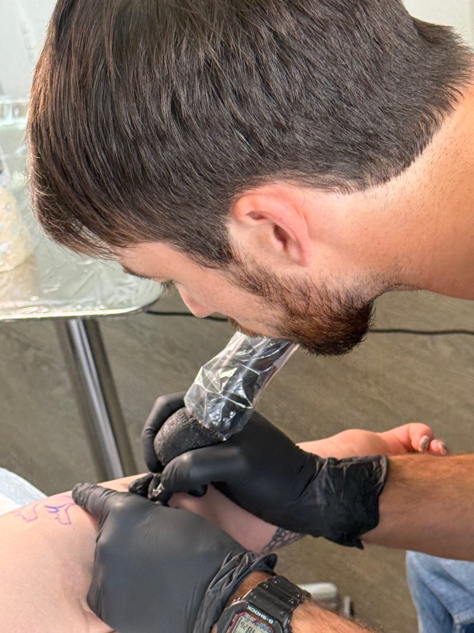 Cade Bennett tattooing overhead angle AK Tattoo Anchorage — focused tattoo artist Alaska